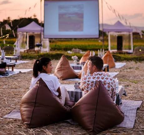 Personas disfrutando de una proyección de cine dominicano al aire libre durante la noche.